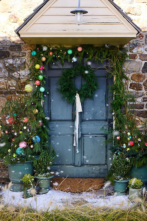 Blue-grey door with cedar garland and pastel ornaments in the snow